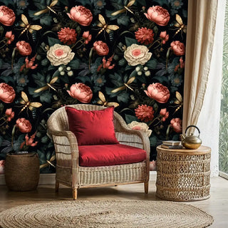 Moody botanical wallpaper with lush flowers and insects in a vintage style, shown in a cozy reading nook with a wicker armchair and red cushion.