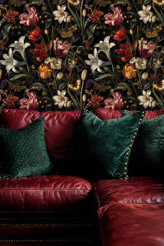 Moody floral wallpaper with lilies and tulips on black, behind a burgundy leather sofa with teal velvet cushions