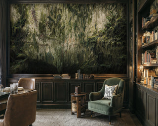 Mossy cliff wall mural with ivy and tropical leaves, framed in a dark study with green armchair and bookshelves