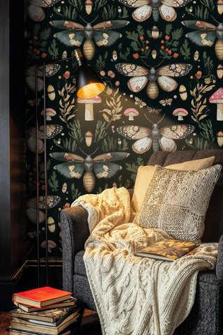 Moth and mushroom wallpaper in earthy tones on black, in a cozy nook with a floor lamp and knit throw
