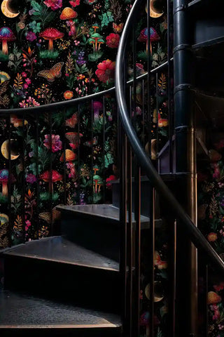 Mystical garden pattern wallpaper on spiral staircase with black metal railings and dramatic lighting