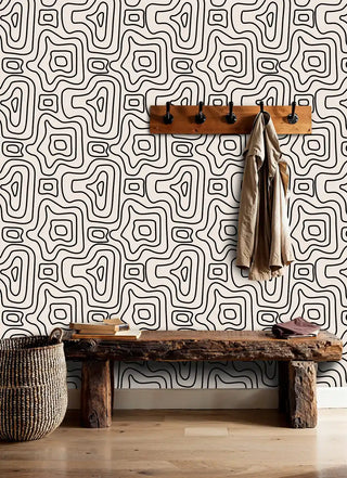 Mystical geometric wallpaper in black and beige shown in rustic entryway with wooden coat rack