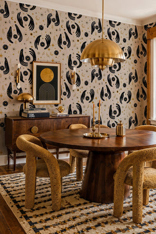 Mystical hands pattern wallpaper with gold celestial motifs in a dining room with round wooden table and pendant