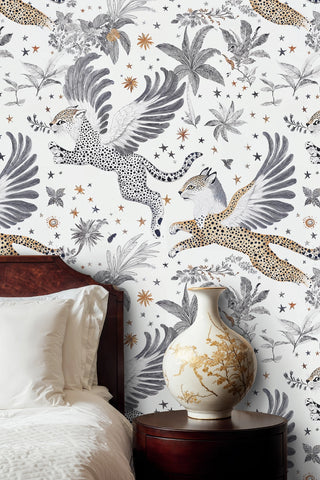 Mythical winged leopard wallpaper with tropical leaves in a bedroom with dark wood headboard and gold vase