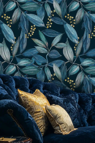 Navy teal botanical leaf wallpaper with gold berries, behind a tufted sofa and gold cushions