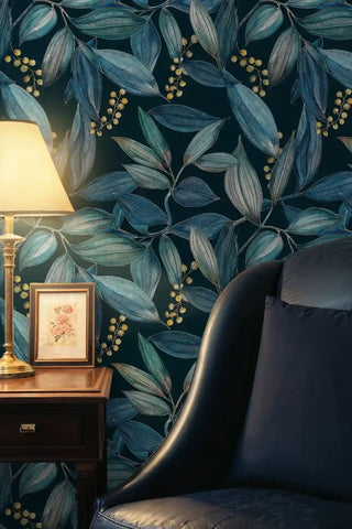 Navy teal botanical leaf wallpaper with gold berries, beside a table lamp and framed art