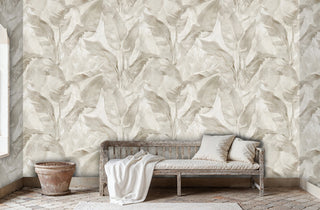 Neutral tropical leaves wallpaper in beige and white tones, displayed in rustic living room with weathered wooden bench