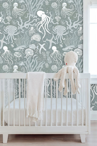 Ocean life wallpaper with jellyfish and sea creatures in green and white, displayed in nursery with white crib