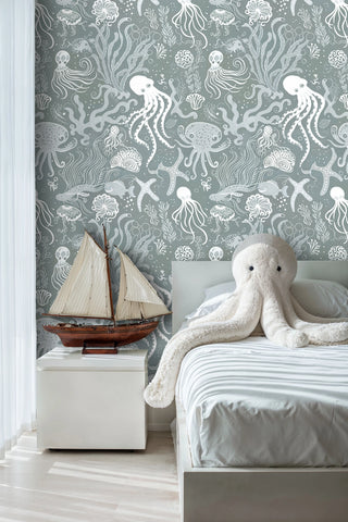 Ocean themed wallpaper with marine life in soft green, shown in kids room with sailboat model