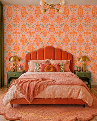 Orange and pink damask wallpaper with crescent moons and green leaves, in a bedroom with scalloped velvet headboard