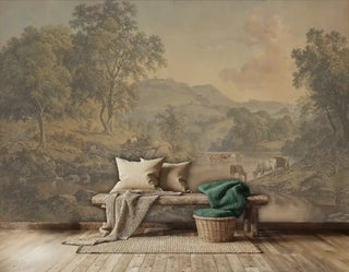 Pastoral landscape wall mural featuring cattle by river, golden trees, and rolling hills in warm earth tones, displayed in rustic living room with wooden bench and green textiles