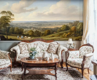Pastoral landscape wall mural with trees and distant village shown in traditional living room with floral furniture