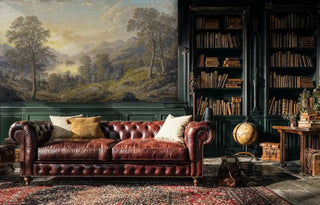 Pastoral landscape wallpaper featuring mountain lake and golden light in a traditional study with leather sofa and bookshelves