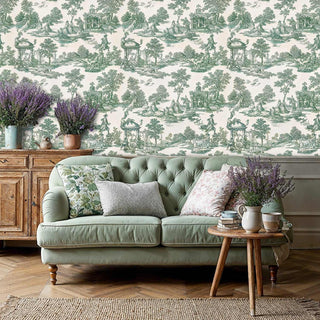 Pastoral toile wallpaper featuring green scenes of figures and pavilions in cream, shown in living room with sage sofa