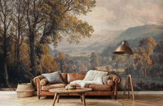 Pastoral valley wall mural with golden autumn trees and misty mountains in warm earth tones, displayed in modern living room with leather sofa