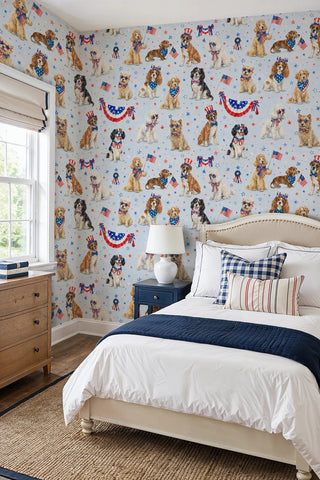 Patriotic dogs wallpaper featuring festive pups and bunting on light blue, shown in a bright bedroom with upholstered headboard.