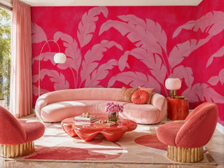 Pink and red banana leaf wallpaper in a maximalist living room with curved pink sofa and gold-base swivel chairs