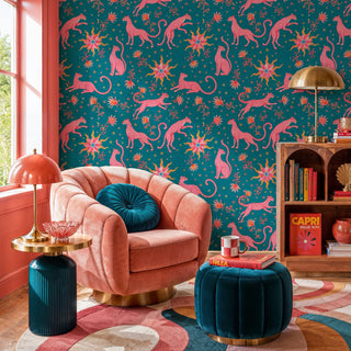 Pink leopard celestial pattern wallpaper on teal, shown in a cozy reading nook with pink armchair and teal pouf