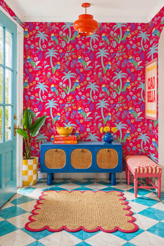 Pink tropical toucan wallpaper with palm trees and florals, in a vibrant entryway with blue cane sideboard