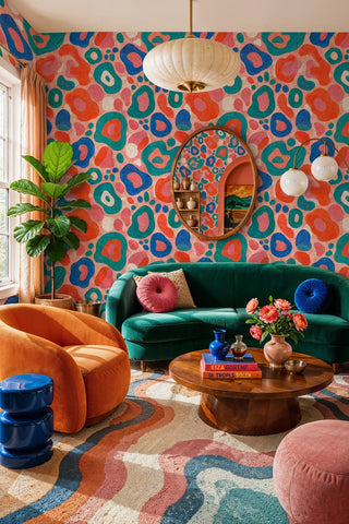 Playful organic blob wallpaper in coral, teal, and blue in a living room with green sofa and orange armchair