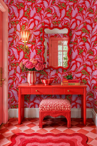 Red acanthus leaf wallpaper with pink swirls and green berries in a bold entryway with wavy mirror