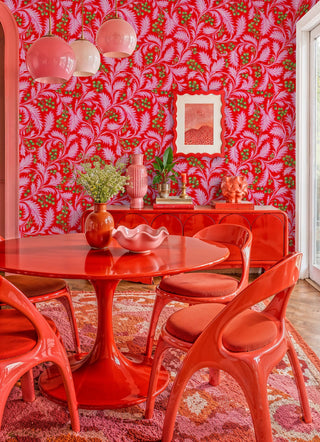 Red and pink swirling foliage wallpaper with green berries in a maximalist dining room with red table