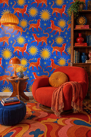 Red wildcat and sun pattern wallpaper on blue, in a cozy reading nook with red armchair and blue pouf
