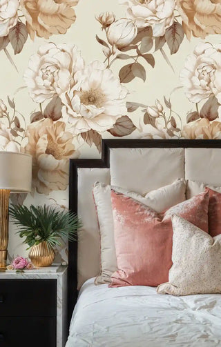Romantic floral wallpaper with oversized blooms in soft beige, shown in bedroom with coral velvet pillows