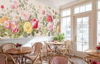 Romantic floral wallpaper with roses and peonies in pink, yellow, and white, shown in charming cafe with wicker chairs