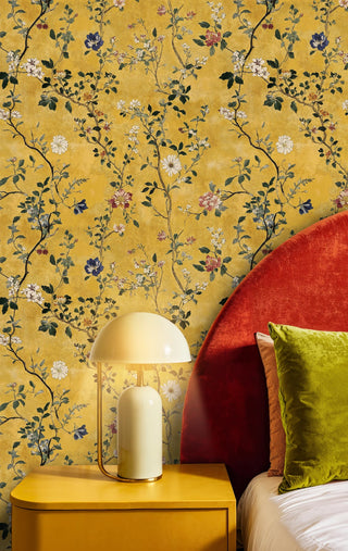 Saffron chinoiserie wallpaper with climbing floral branches, in a modern bedroom with red headboard and mushroom lamp