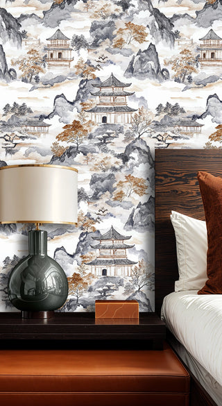 Scenic pagoda wallpaper in grey and amber tones in a modern bedroom with green glass lamp and leather bench