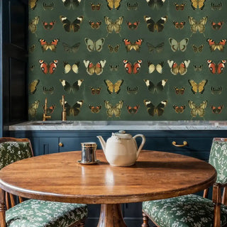 Scientific butterfly illustration wallpaper used as a backsplash in a dark, classic kitchen with a round wooden dining table.