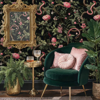 Serpentine garden wallpaper featuring pink florals and snakes on black, in luxurious room with emerald velvet chair