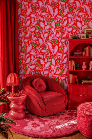 Swirling pink leaf wallpaper on red background with green berries in a cozy reading nook with red armchair
