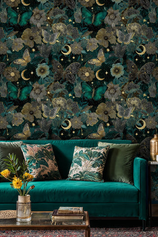 Teal and gold celestial butterfly wallpaper with lush florals behind an emerald velvet sofa with botanical pillows