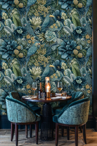 Teal botanical wallpaper featuring parrots and large blooms shown in an intimate dining booth with velvet chairs and candles