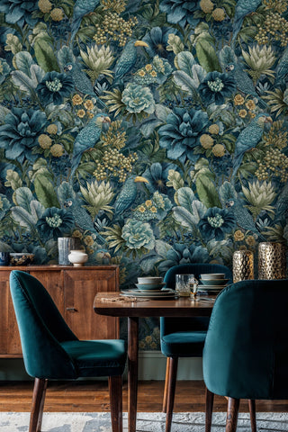 Teal tropical bird wallpaper with dense foliage in a dining room with velvet chairs, wooden sideboard and gold vases