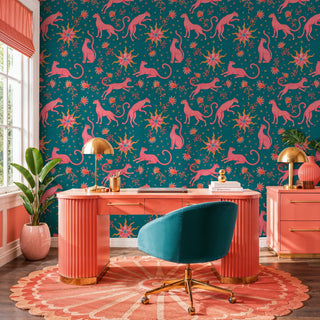 Teal wallpaper with pink leopards and celestial suns, displayed in a home office with coral desk and teal chair
