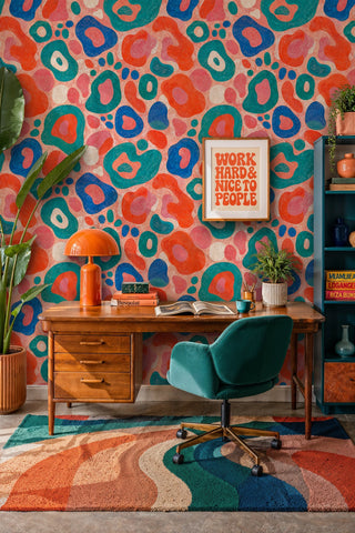 Textured abstract shapes wallpaper in vibrant hues shown in a home office with wooden desk and teal chair
