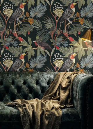 Toucan and foliage wallpaper on dark background shown in moody living room with tufted velvet sofa and throw blanket