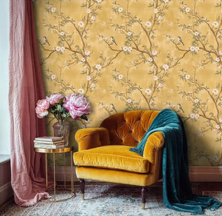 Traditional chinoiserie wallpaper featuring songbirds and blossoms, styled in cozy reading nook with mustard velvet armchair
