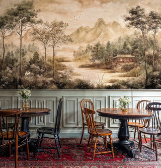 Traditional mountain scene wall mural in beige and green tones, shown in rustic dining space with antique chairs
