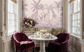 Tropical animal wall mural featuring giraffes and zebras in pink tones, shown in dining room with burgundy velvet chairs and marble table