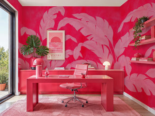 Tropical banana leaf wallpaper in vibrant red and pink tones displayed in a modern home office with coral desk