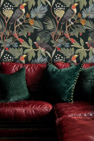 Tropical bird wallpaper featuring toucans and palm fronds on dark background, displayed behind burgundy leather sofa