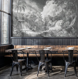Tropical engraving wall mural with waterfalls and palm trees in grey tones, in an industrial cafe with rustic wood table
