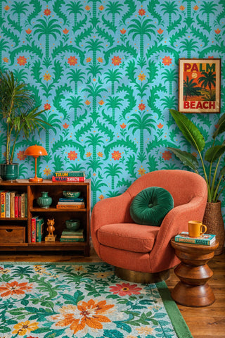 Tropical palm damask wallpaper with green foliage and orange blooms on blue, in a retro lounge with coral armchair