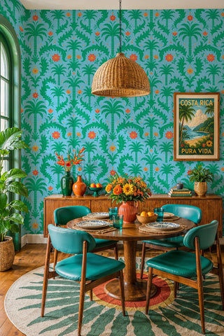 Tropical palm floral wallpaper in green and sky blue with orange flowers, shown in a dining room with rattan pendant