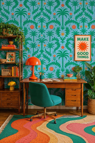 Tropical palm leaf wallpaper with orange florals on sky blue, in a home office with vintage wooden desk