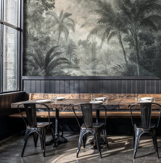 Tropical palm tree wall mural in muted green and beige, displayed in an industrial cafe with metal chairs